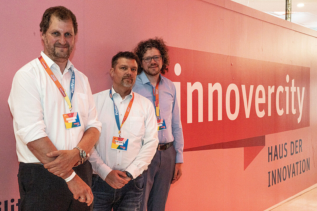 Drei Männer lehnen sich gegen einer rote Wand mit dem rotweißen innovercity Festival-Logo. 